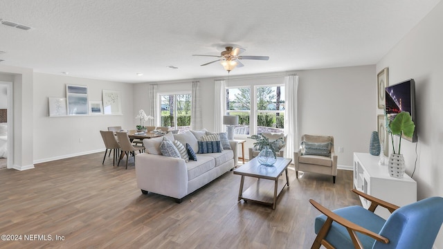 living room featuring a textured ceiling, baseboards, visible vents, ceiling fan, and wood finished floors