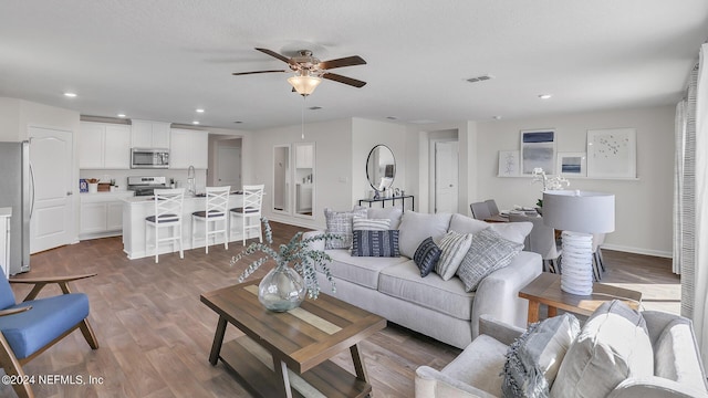living room featuring wood finished floors, a ceiling fan, visible vents, and recessed lighting