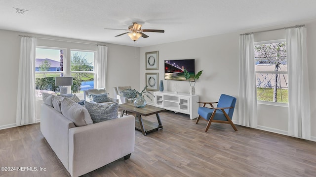 living area with a wealth of natural light, a ceiling fan, visible vents, and wood finished floors