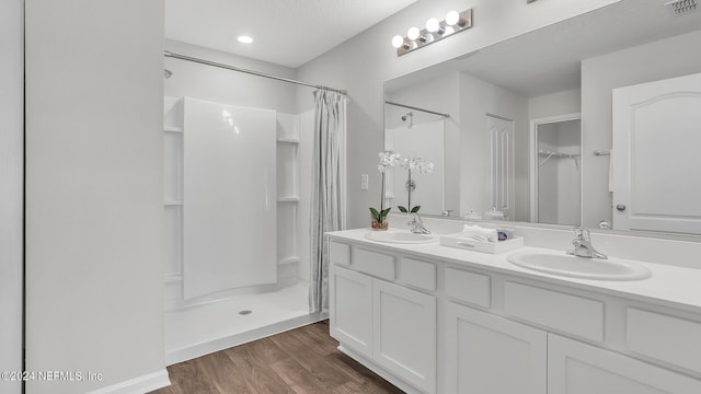 bathroom featuring a sink, double vanity, a shower stall, and wood finished floors