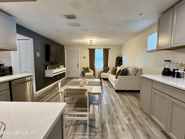 interior space with light wood-style floors, stainless steel dishwasher, gray cabinets, and visible vents