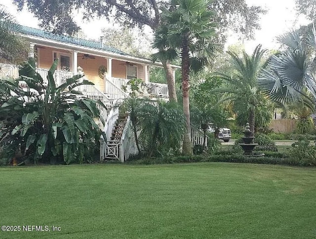 view of green lawn with a porch and stairway