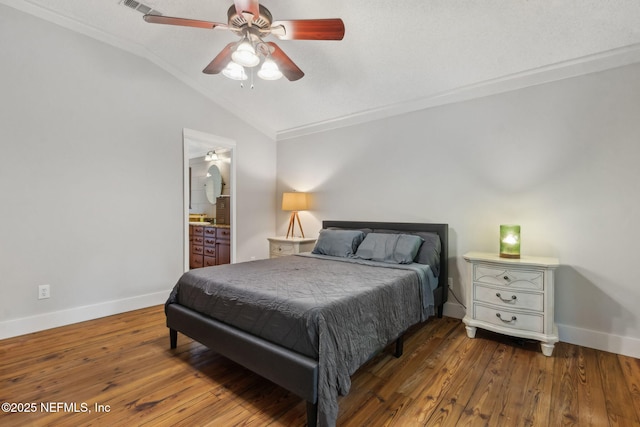 bedroom with vaulted ceiling, baseboards, ornamental molding, wood finished floors, and ensuite bath