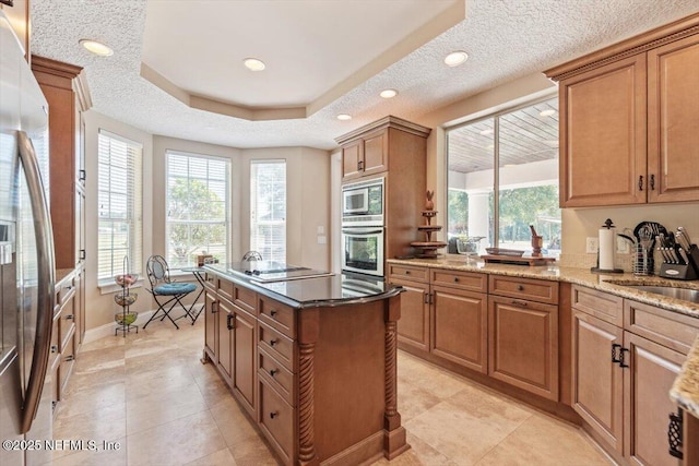 kitchen featuring stainless steel appliances, a kitchen island, light stone countertops, brown cabinets, and baseboards