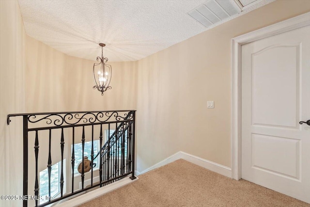 interior space with a textured ceiling, carpet, baseboards, visible vents, and a chandelier