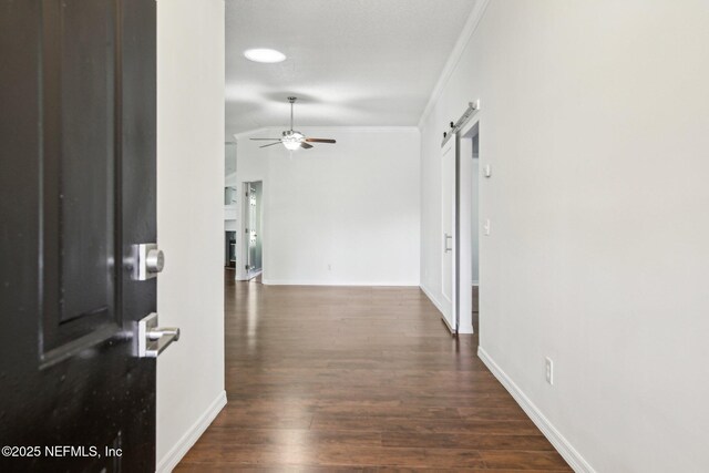 hallway with ornamental molding, a barn door, dark wood-style flooring, and baseboards