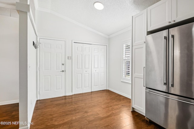 foyer entrance with vaulted ceiling, a textured ceiling, dark wood-style flooring, ornamental molding, and baseboards