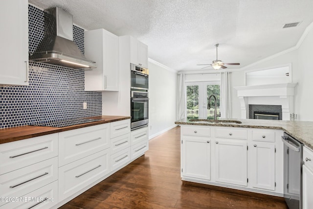 kitchen with wall chimney exhaust hood, wooden counters, appliances with stainless steel finishes, a sink, and ceiling fan