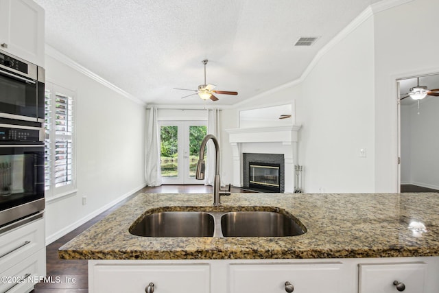 kitchen featuring ceiling fan, a sink, stainless steel oven, dark stone countertops, and ornamental molding