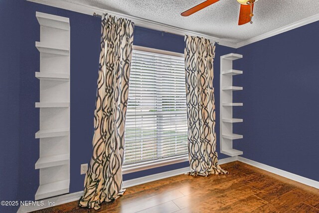 spare room with ceiling fan, a textured ceiling, wood finished floors, crown molding, and baseboards