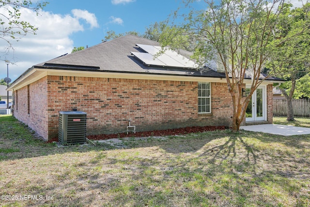 view of property exterior featuring central air condition unit, brick siding, roof mounted solar panels, and french doors
