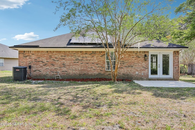 rear view of house with brick siding, central AC unit, a yard, and roof mounted solar panels