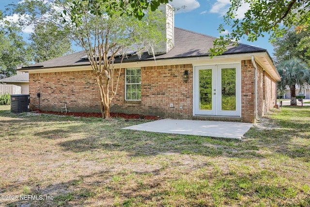 rear view of house featuring central AC unit, a patio area, a yard, a chimney, and brick siding