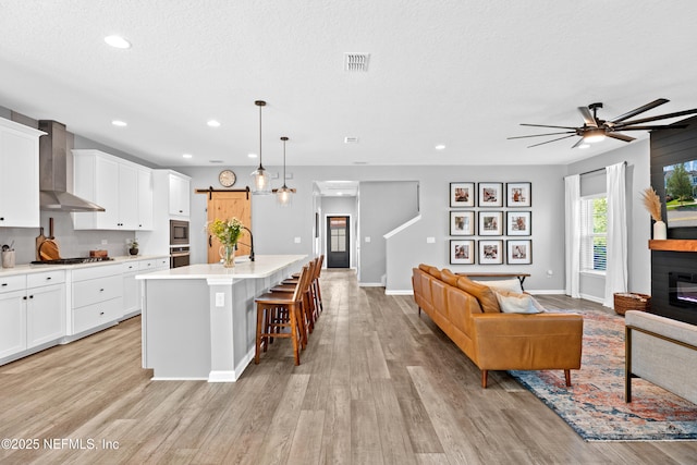 kitchen with wall chimney range hood, appliances with stainless steel finishes, ceiling fan, a barn door, and open floor plan