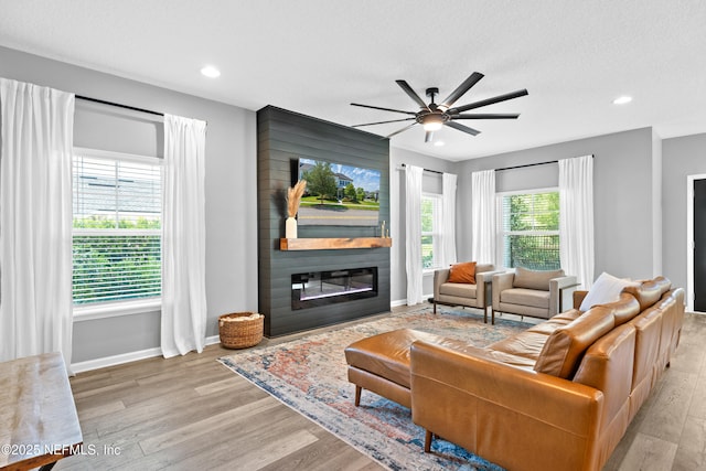 living area featuring light wood-type flooring, a large fireplace, ceiling fan, recessed lighting, and baseboards