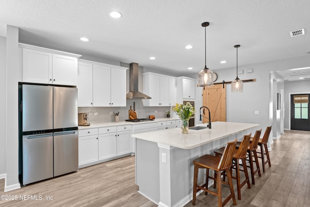 kitchen with freestanding refrigerator, wall chimney range hood, a sink, a barn door, and light wood-style floors