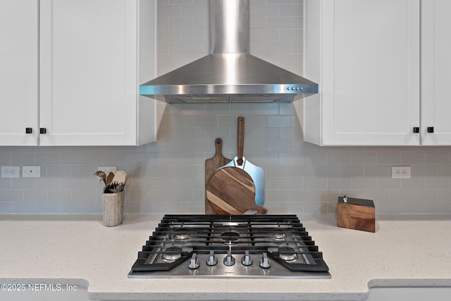kitchen view of wall chimney exhaust hood, stainless steel gas stovetop, tasteful backsplash, and white cabinets