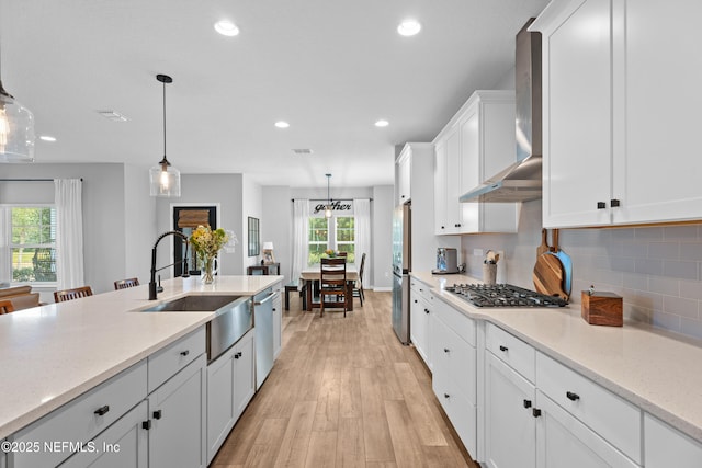 kitchen with a sink, appliances with stainless steel finishes, wall chimney exhaust hood, white cabinetry, and recessed lighting