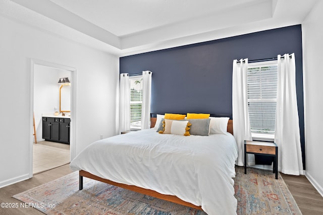bedroom featuring a raised ceiling, light wood-type flooring, and multiple windows