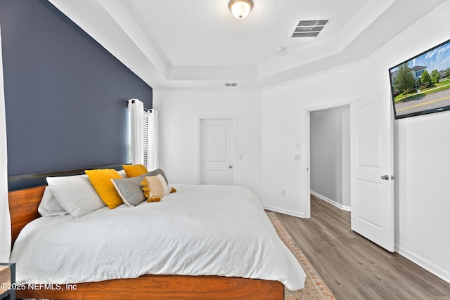 bedroom with a raised ceiling, wood finished floors, and baseboards
