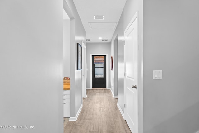 corridor featuring baseboards, light wood-style flooring, and attic access