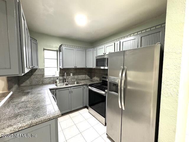 6332 Badnur Dr, Jacksonville, FL 32210 - kitchen with stainless steel appliances, a sink, gray cabinets, backsplash, and light tile patterned floors