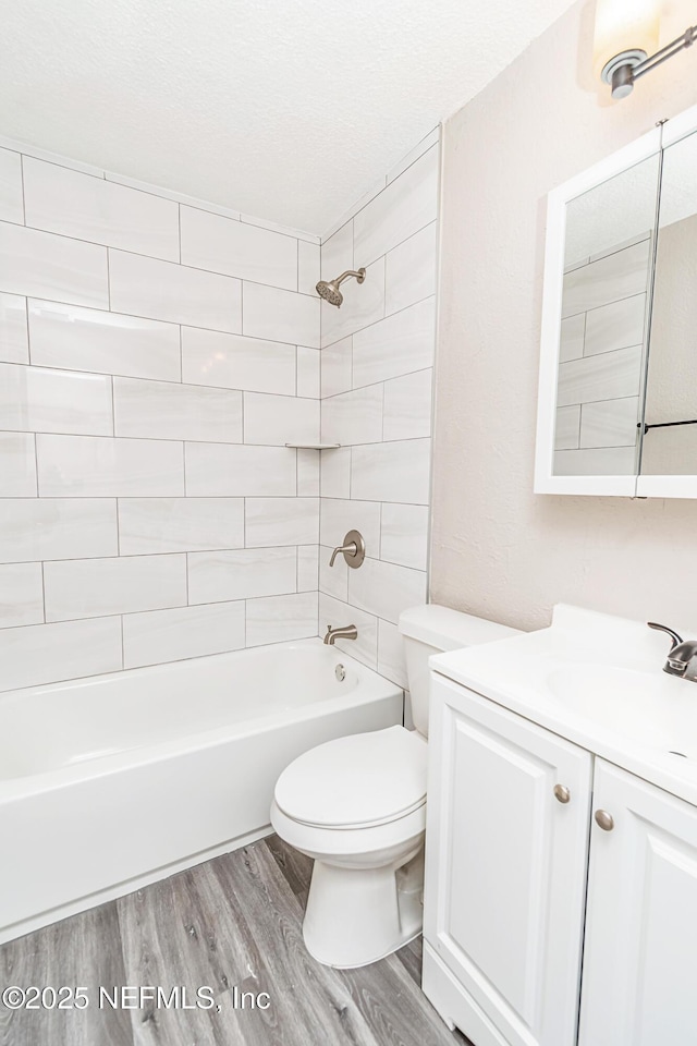 full bath with toilet, wood finished floors, vanity, a textured ceiling, and bathtub / shower combination