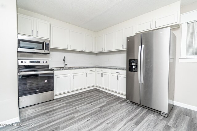 610 S 9th St, Macclenny, FL 32063 - kitchen featuring baseboards, decorative backsplash, light wood-style floors, stainless steel appliances, and white cabinets