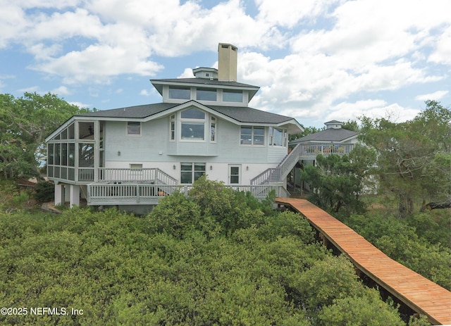 back of property with a chimney, a sunroom, stairway, and a wooden deck