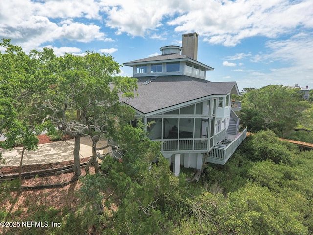 back of property with roof with shingles, a chimney, and a sunroom