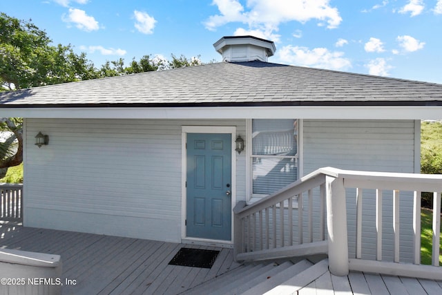 view of exterior entry featuring roof with shingles and a deck