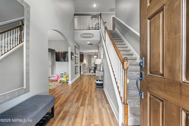 foyer featuring stairway, light wood-style flooring, a high ceiling, arched walkways, and baseboards