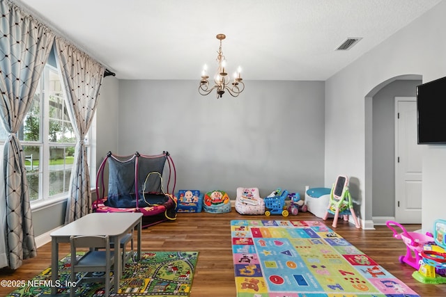 game room featuring arched walkways, a chandelier, wood finished floors, and baseboards