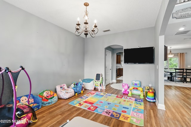 rec room featuring arched walkways, wood finished floors, a chandelier, and baseboards