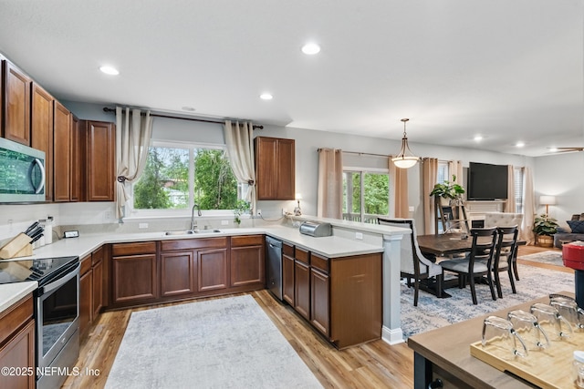 kitchen with stainless steel appliances, a sink, a peninsula, light wood-style floors, and open floor plan