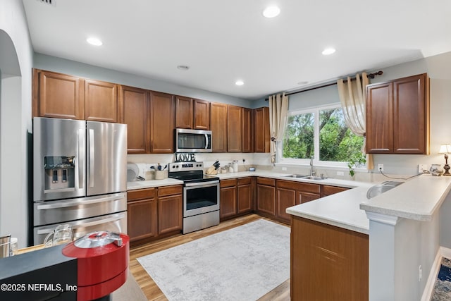 kitchen featuring appliances with stainless steel finishes, a sink, a peninsula, light wood-style flooring, and light countertops