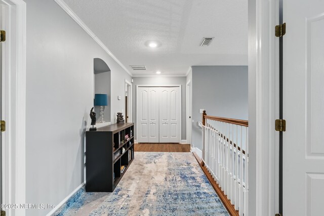 hallway featuring ornamental molding, arched walkways, baseboards, wood finished floors, and a textured ceiling
