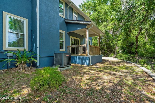 view of side of property with a ceiling fan, cooling unit, a porch, and stucco siding