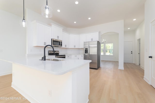 kitchen with appliances with stainless steel finishes, a sink, light countertops, light wood-type flooring, and a peninsula