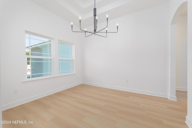 unfurnished dining area featuring arched walkways, a chandelier, light wood-style flooring, and baseboards