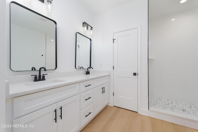 bathroom featuring wood finished floors, double vanity, tiled shower, and recessed lighting