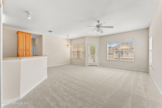 empty room featuring light carpet, a textured ceiling, baseboards, a ceiling fan, and a chandelier