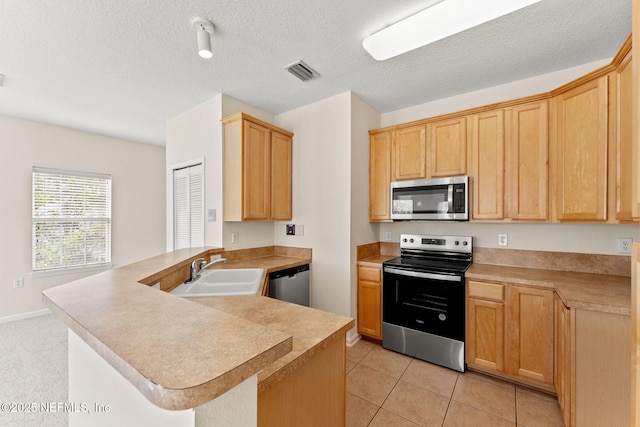 kitchen featuring appliances with stainless steel finishes, a sink, a peninsula, light countertops, and light brown cabinets