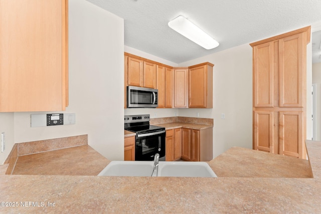 kitchen with appliances with stainless steel finishes, a sink, light countertops, and light brown cabinetry