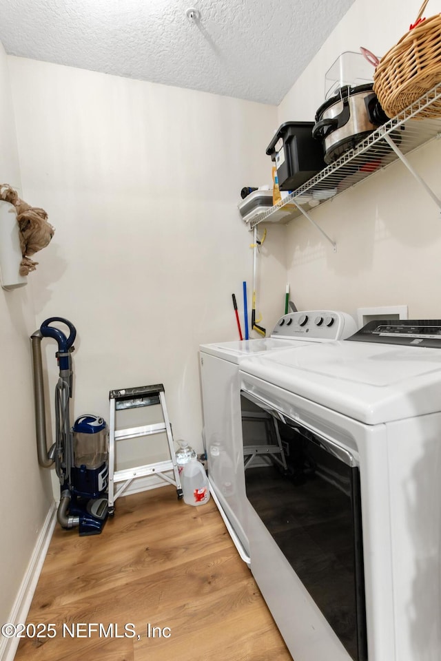 washroom with light wood-style flooring, a textured ceiling, baseboards, washing machine and clothes dryer, and laundry area