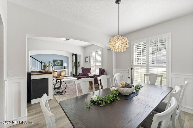 11698 Donato Dr, Jacksonville, FL 32226 - dining area with arched walkways, a decorative wall, light wood-type flooring, a wainscoted wall, and a textured ceiling