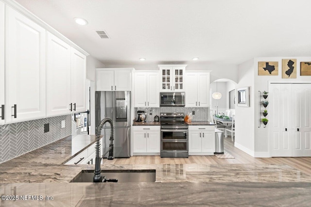 11698 Donato Dr, Jacksonville, FL 32226 - kitchen with stainless steel appliances, decorative backsplash, arched walkways, white cabinetry, and glass insert cabinets