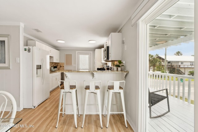 2902 W 5th St, Fernandina Beach, FL 32034 - kitchen featuring white fridge with ice dispenser, stainless steel microwave, a peninsula, white cabinetry, and light wood-style flooring