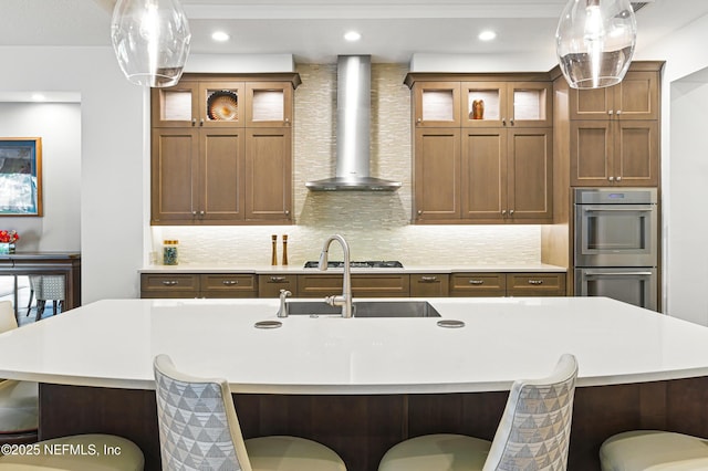 120 Hallowes Cv, Saint Johns, FL 32259 - kitchen with wall chimney exhaust hood, light countertops, appliances with stainless steel finishes, a breakfast bar area, and an island with sink