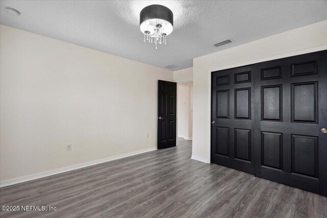 3357 Pegaso Ave, New Smyrna Beach, FL 32168 - unfurnished bedroom with dark wood finished floors, a textured ceiling, baseboards, a chandelier, and a closet